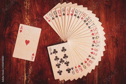 Photography Deck of playing cards arranged in circular stack or design or pattern with ace of hearts aside on a wooden background for performing illusion or magic trick