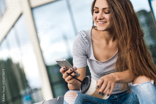 Woman using phone sitting near mall with coffee after shopping.