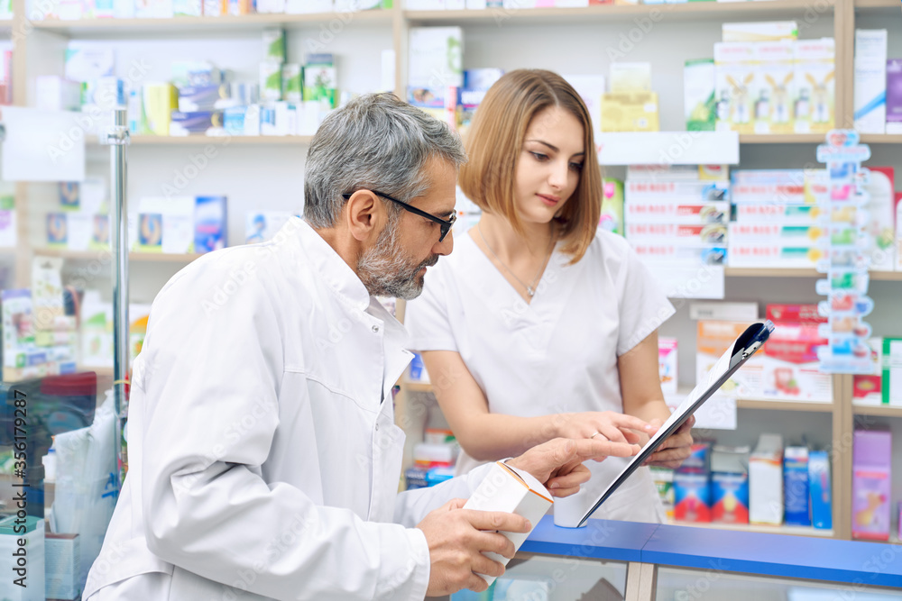Two pharmacist checking product in folder. Two pharmacist checking product in folder.