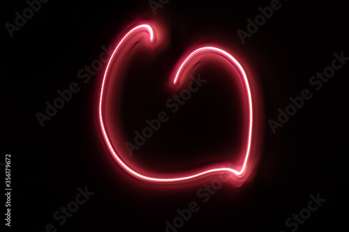 Abstract pink light painting photography, long exposure shot of glowing neon heart love against a black background.