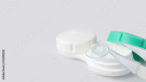 White container case for contact lenses, tweezers on a light gray background close-up. The concept of poor vision, hyperopia, myopia