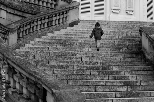 Obraz na plátne Unrecognisable little girl, modern-day lonely princess walking up majestic curved stairs of empty castle in Europe