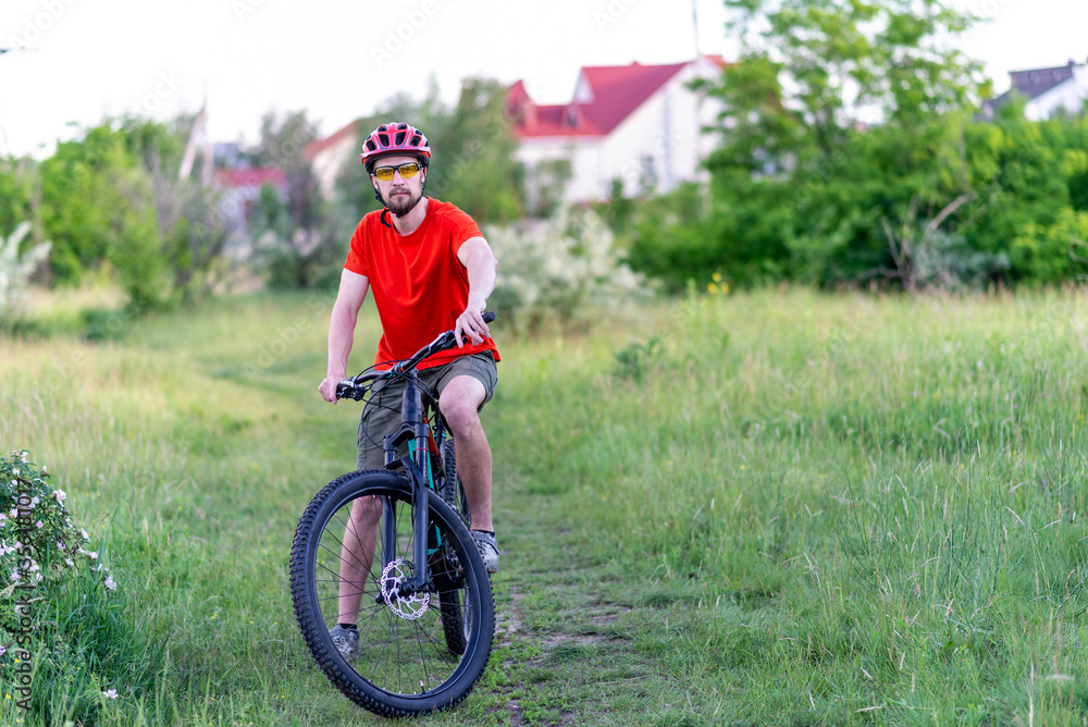 Fototapeta premium A cyclist in a bright orange t-shirt stands with a mountain bike.