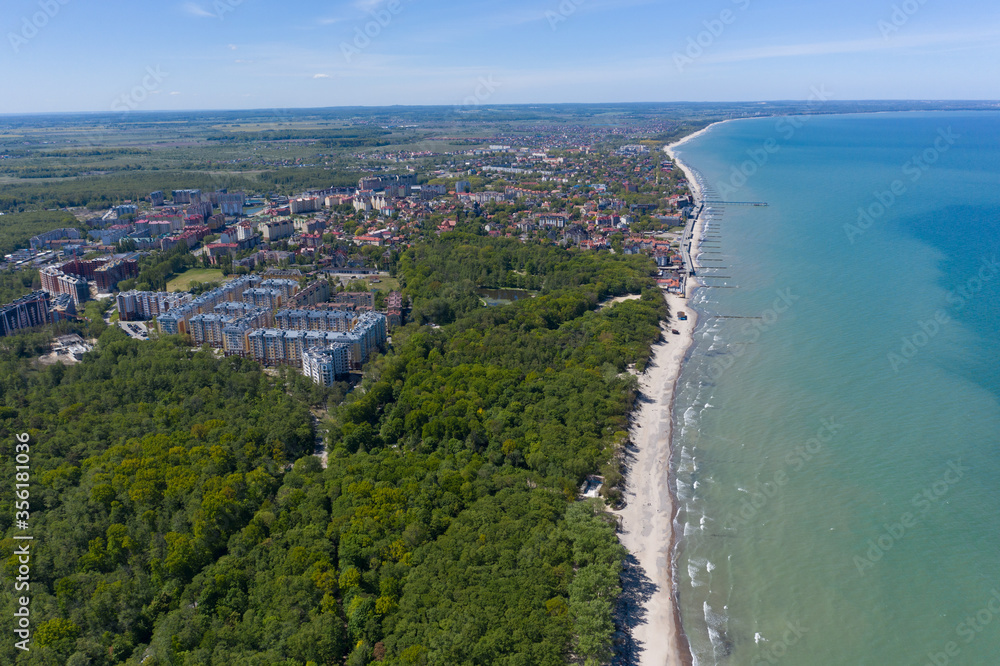 Top view of the Baltic sea coast. You can see the resort town of Zelenogradsk, the promenade, the blue sea and the sandy strip of beach stretching into the distance.