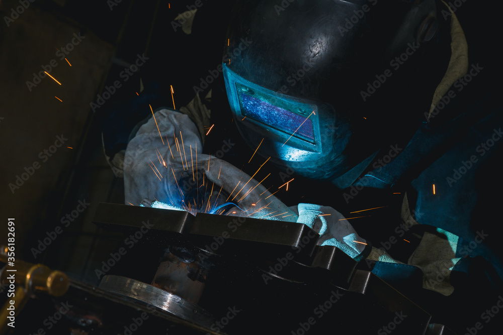 Close-up blacksmith welder in protective mask works with metal steel and iron using a welding machine, bright sparks and flashes. Welder uses a mask to protect your eyes from sparks. Close-up blacksmith welder in protective mask works with metal steel and iron using a welding machine, bright sparks and flashes. Welder uses a mask to protect your eyes from sparks.