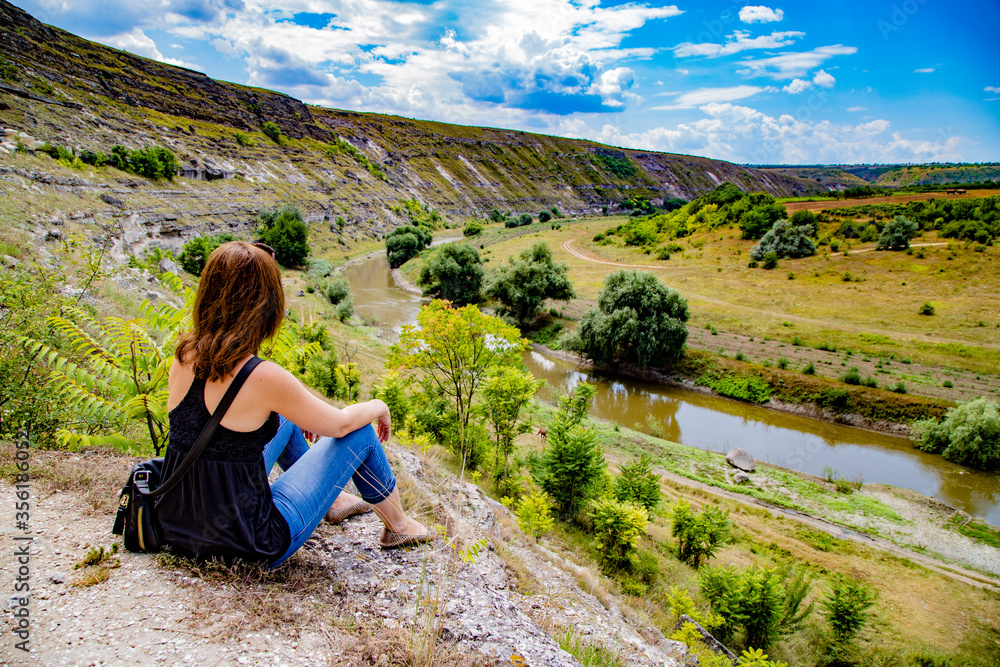 Naklejka premium Young woman sitting on the top of the hill and looking at the Old Orhei. Historical and archaeological complex, located in Trebujeni. Moldova. July 2019.