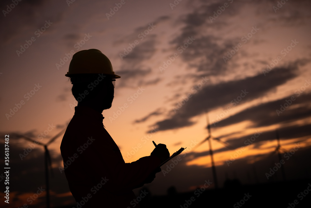 Silhouette of man engineer working and holding the report at wind turbine farm Power Generator Station on mountain,Thailand people Silhouette of man engineer working and holding the report at wind turbine farm Power Generator Station on mountain,Thailand people