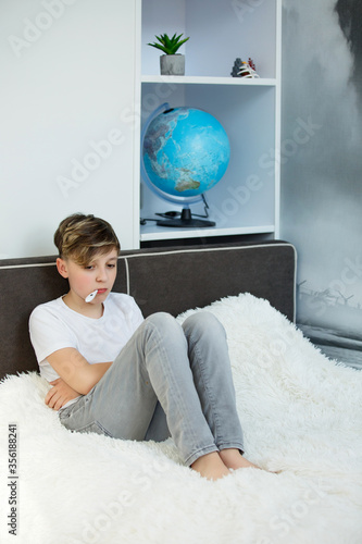 Sick boy with thermometer in his mouth sitting on the bed , great design. Temperature check. Virus concept.