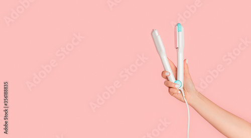 Girl hand holding hair straightener on pink background, blank space photo