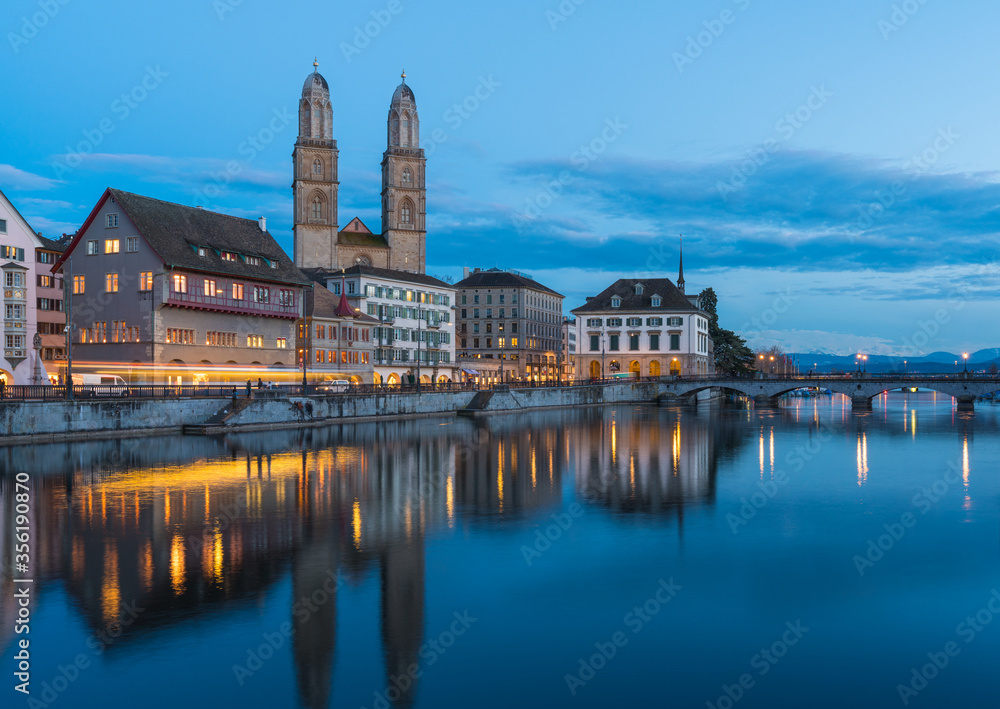 Zurich cathedral reflected on the calm waters of the river, after sunset