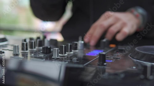 DJ sound control console for mixing dance music and laptop in disco club. Hands touching buttons sliders, playing electronic music on mixing deck, color illumination in nightclub dance party. Close up