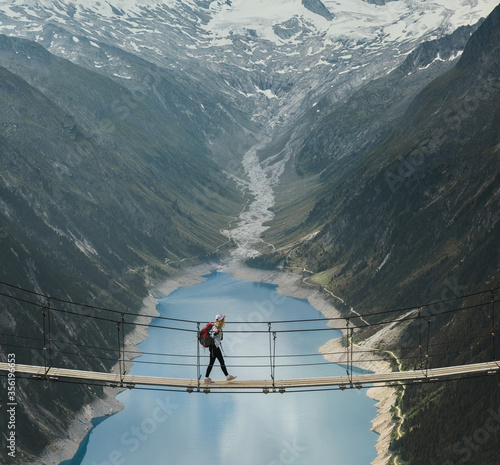 Girl traveler with a backpack in the mountains. A young girl stands on a suspension bridge on a background of mountains and glaciers. Travel and active life concept. Adventure trip to Europe.