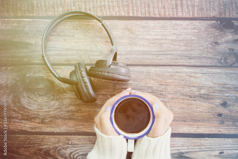Top view of female hands holding cup of coffee and the headphone on wooden table. Top view of female hands holding cup of coffee and the headphone on wooden table.