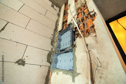 Electrical cables laid to plastic fusebox installed on the wall in a room under construction works. © bilanol