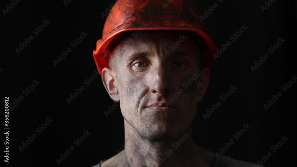 The face of a male miner in a helmet on a black background. Portrait of a mining worker. The face of a male miner in a helmet on a black background. Portrait of a mining worker.