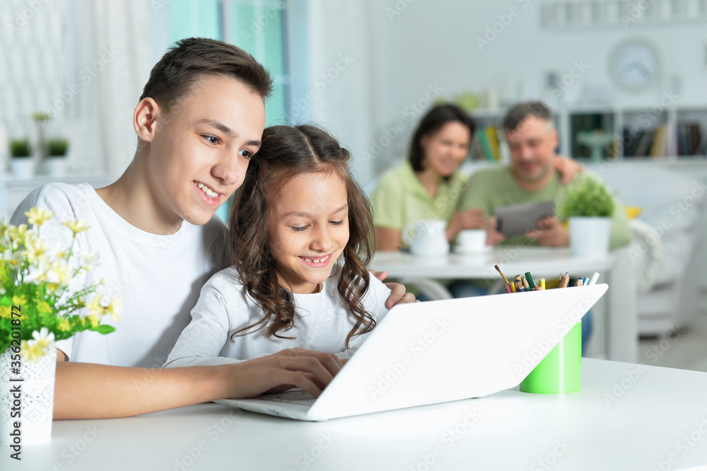 Brother and sister using laptop while sitting at table Brother and sister using laptop while sitting at table