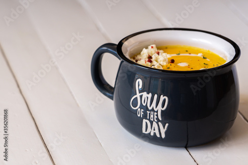 Pumpkin soup in a blue bowl isolated. Inscription: soup of the day. Vegetarian lunch or dinner. Healthy food concept. Copy space. 