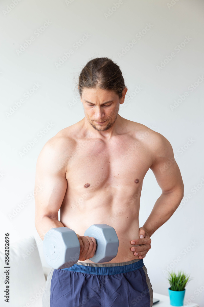 Obraz premium Athletic young man doing exercise with dumbbell in living room at home