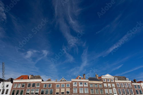 Top parts of exterior facades of canal mansions in Middelburg with vast white space blue sky with swirling cloud patches