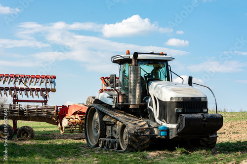 A very large white crawler tractor stands in a field in summer while cultivating agricultural land © Niko_Dali