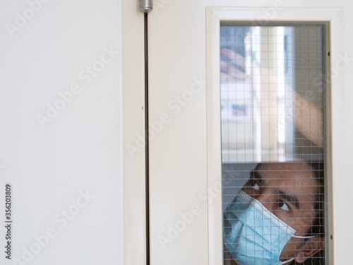 Lonely man in medical mask looking through the window. Isolation at home for self quarantine. Concept home quarantine, prevention COVID-19. Coronavirus outbreak situation