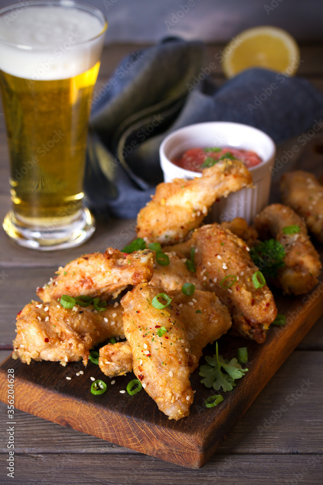 Crispy chicken wings with sauce and glass of lager beer. Vertical image