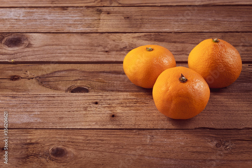 Three fresh tangerines lie on a wooden background