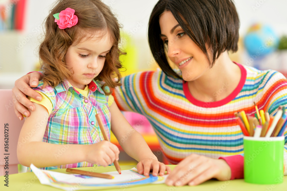 Little cute girl with mother drawing at the table at home