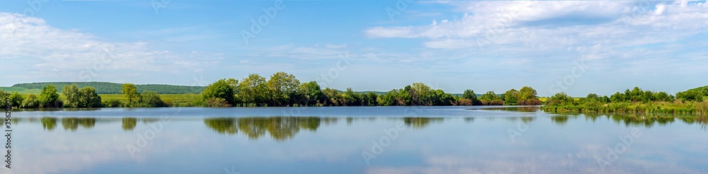 Wide panorama, summer landscape with river and trees reflected in water in sunny weather