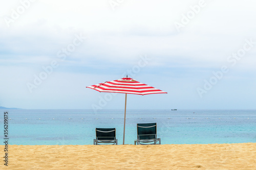 Idyllic tropical Caribbean island summer beach vacation setting. Two empty lounge/ sun chairs under large red & white striped patio umbrella on beautiful white sand by the ocean in Montego Bay Jamaica photo