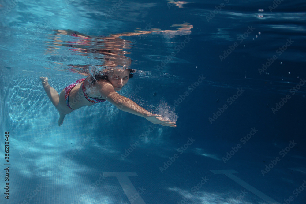 A woman swimming in the pool and diving in the pool, enjoying the pool and the summer. The girl is diving in the pool and is wearing a bikini