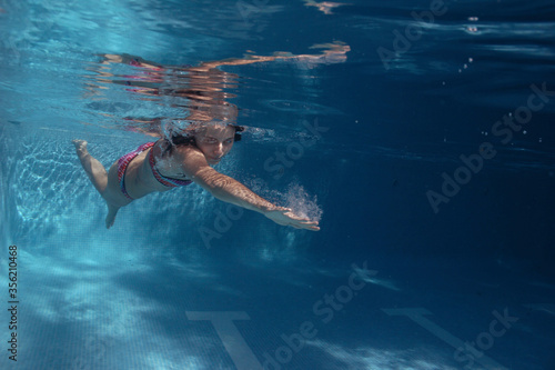 A woman swimming in the pool and diving in the pool, enjoying the pool and the summer. The girl is diving in the pool and is wearing a bikini
