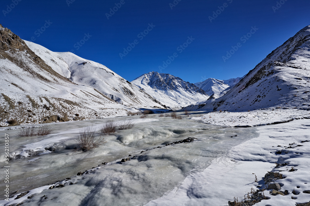 Road to Rumbak Valley and Yarutse, Hemis NP, Ladak, India. River with snow during winter, Himalayas. Mountain landscape in India wild nature. Sunny day with snow in the valley, blue sky with clouds.