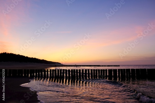 Beautiful sunset colors on the beach of sea. Silhouette of breakwater on foreground.
