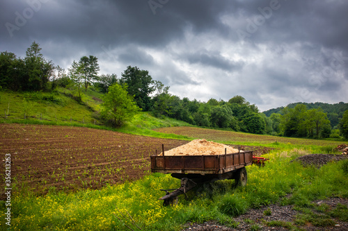 Old tractor trailer on agriculture field. Springtime, cloudy day with dramatic sky.