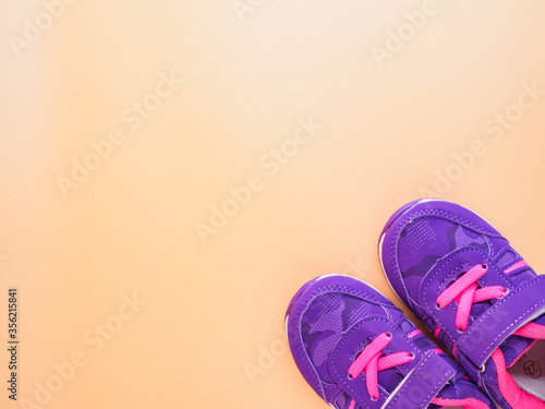 Top view of violet pink childrens sneakers with laces and clasps fasteners at peach background with place for text photo