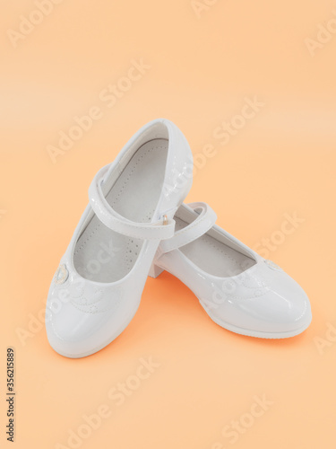 Pair of white baby lacquered girls shoes at peach background