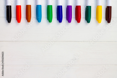 Multi-colored markers on a white wooden background. Top view. Copy space.