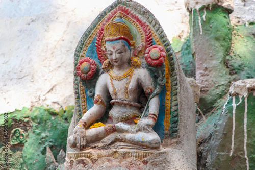 Old stone Buddha statue in Kathmandu city, Nepal. Buddha sits in lotus position (Padmasana). Religious architecture theme.