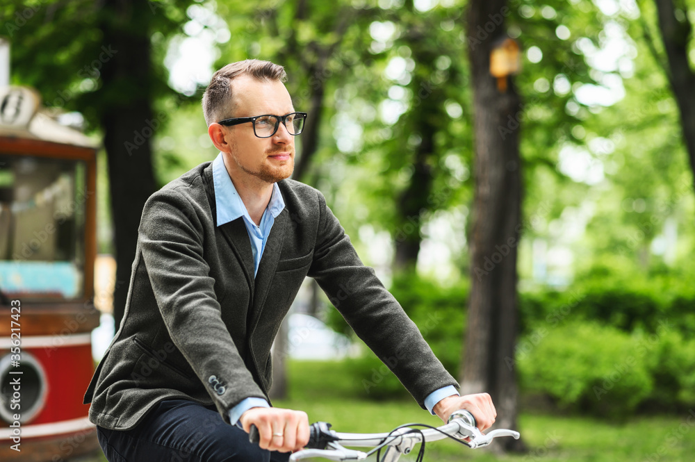 Attractive guy gets to office on a bicycle. Young man in stylish smart casual clothes rides on a bike