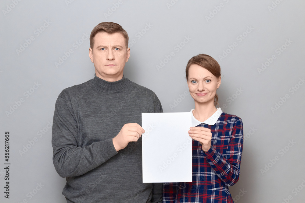 Portrait of adult couple holding together white blank paper sheet Portrait of adult couple holding together white blank paper sheet