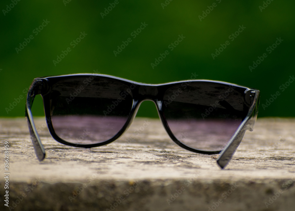 Forgotten sunglasses. Black sunglasses on a stone. Green background. Close up
