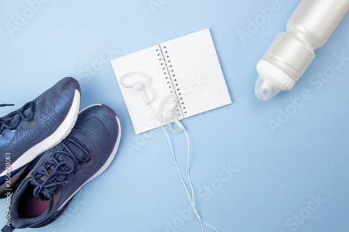Sports layout. Fitness accessories sneakers, earphones and notebook on a blue background. I do sports and fitness at home.