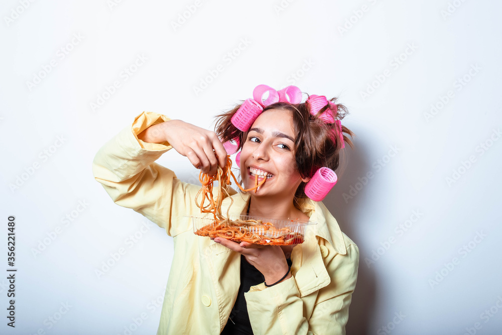 Curly girl in clothes and a plate with pasta and a fork wildly eats pasta with ketchup, standing in glasses on a white background. Girl eating spaghetti. Girl holding a plate of pasta.