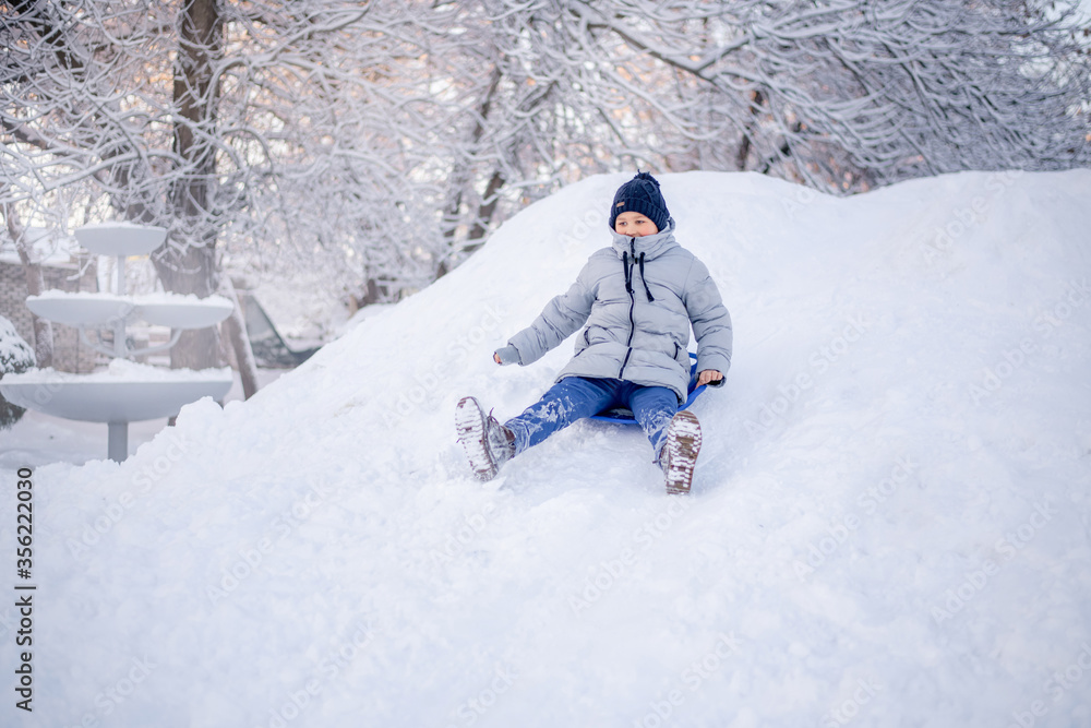 Winter fun in the city. A boy rides on a slide of ice.