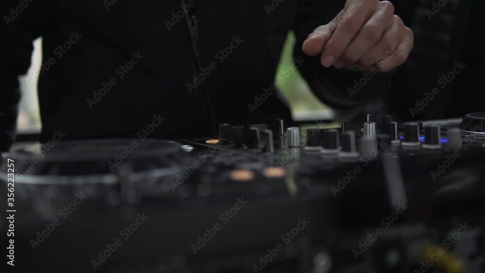 DJ sound control console for mixing dance music and laptop in disco club. Hands touching buttons sliders, playing electronic music on mixing deck, color illumination in nightclub dance party. Close up DJ sound control console for mixing dance music and laptop in disco club. Hands touching buttons sliders, playing electronic music on mixing deck, color illumination in nightclub dance party. Close up