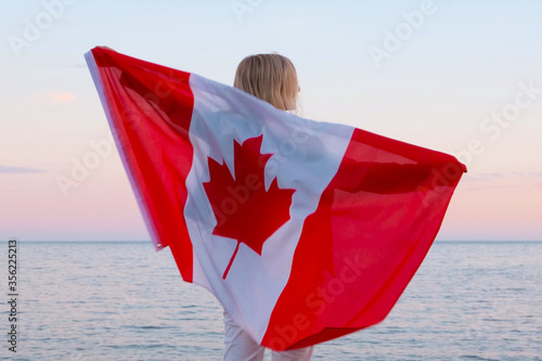 Картината върху платно Back view woman waving national canada flag outdoors ocean sea sunset at summer