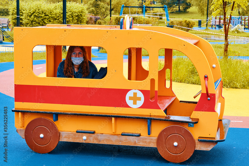 Woman in a medical mask on a children playground in a toy ambulance