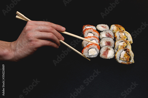 Sushi set on a black plate background. hand holds a roll of chopsticks