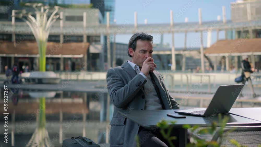 WS Businessman using laptop and drinking coffee in sidewalk cafe in business district / Milan, Italy WS Businessman using laptop and drinking coffee in sidewalk cafe in business district / Milan, Italy